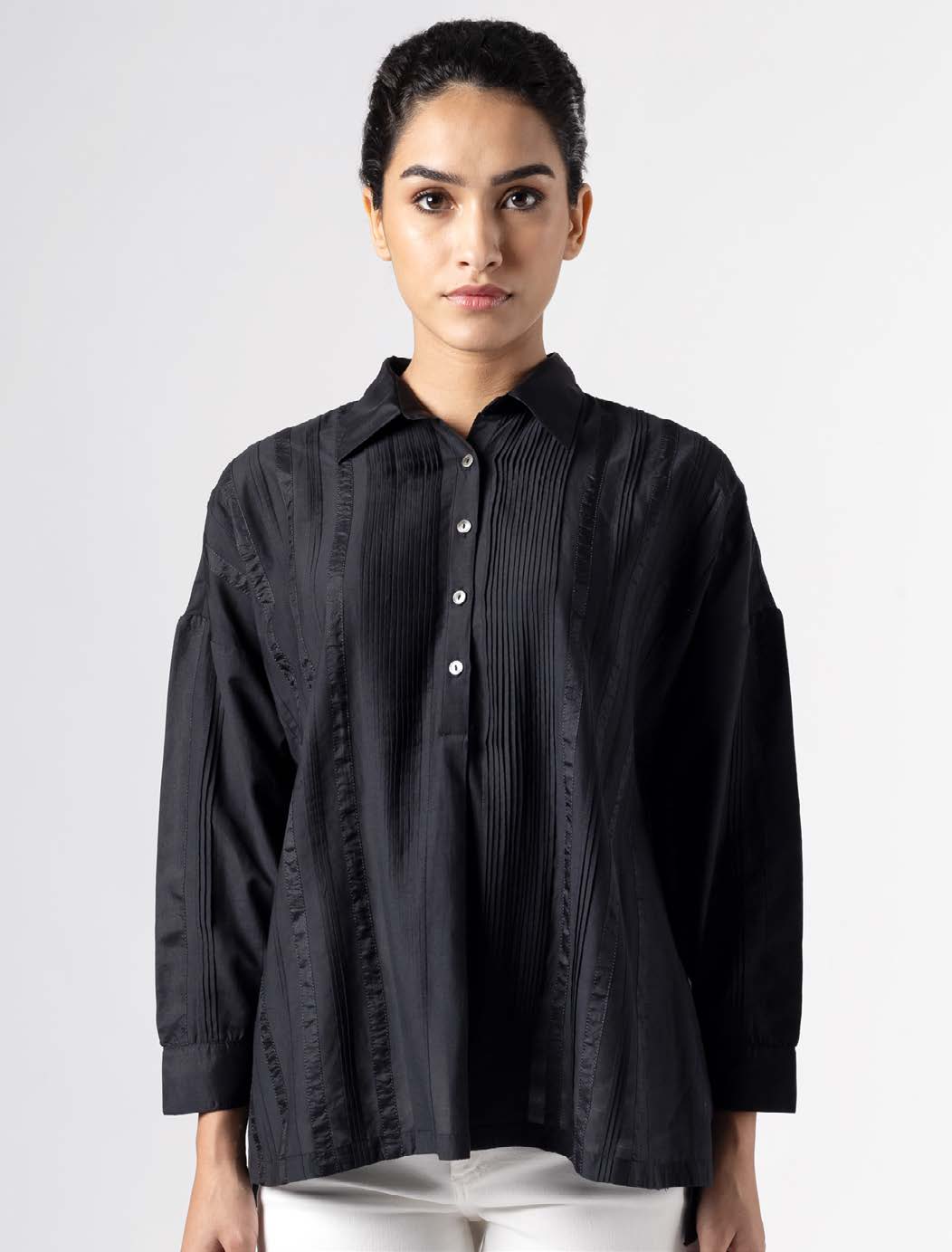 Black pleated blouse with a button-up front, worn by a model against a plain background. Highlights modern, versatile fashion suitable for various occasions.
