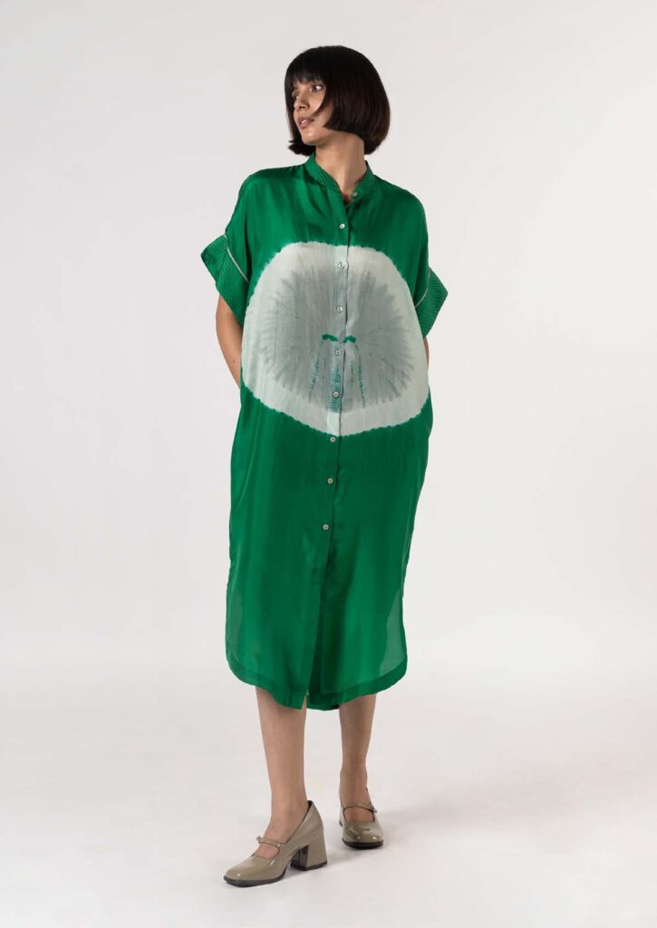 Woman wearing a vibrant green shirt dress with a unique white pattern, posed in a minimalist setting, showcasing contemporary fashion.